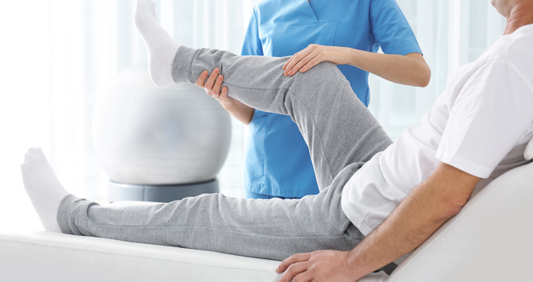 Doctor in blue shirt stretching patient in gray sweatpants