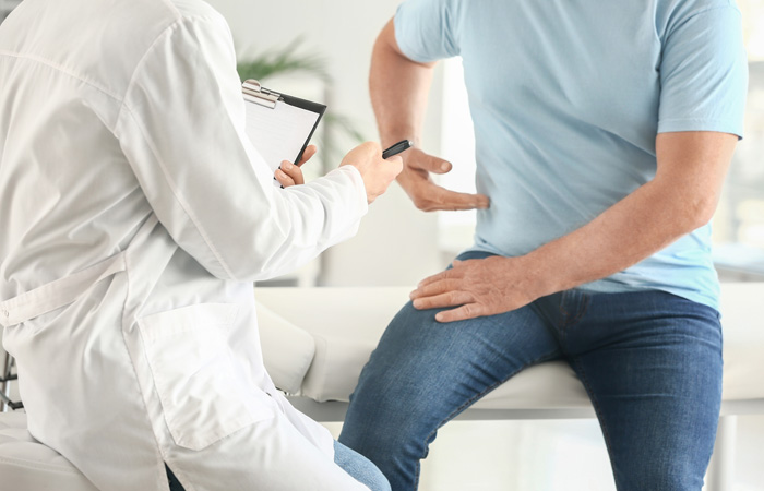 Man in blue t-shirt and jeans pointing to his abdomen while doctor inspects